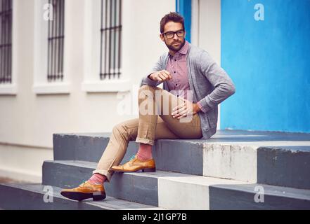 Manchmal sind die Straßen der Stadt meine Inspiration. Aufnahme eines hübschen jungen Mannes, der auf einer Treppe draußen in der Stadt sitzt, während er tief in Gedanken ist. Stockfoto