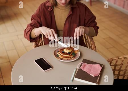 Horizontale High-Angle-Aufnahme der jungen kaukasischen Frau, die köstliche Pfannkuchen im modernen Café isst, Kopierraum Stockfoto