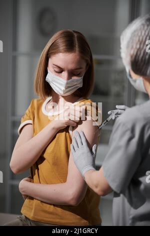 Vertikale Aufnahme eines nicht erkennbaren Arztes, der persönliche Schutzausrüstung trägt und eine Spritze hält, die den Patienten impft Stockfoto