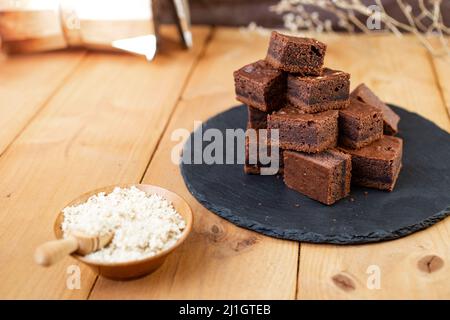 Brownie-Quadrate auf einer schwarzen Steinplatte neben einer Schüssel voller gehackter Walnüsse gestapelt Stockfoto