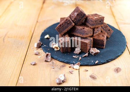 Brownie-Würfel und zerbröckelte Schokolade auf einer schwarzen Steinplatte Stockfoto