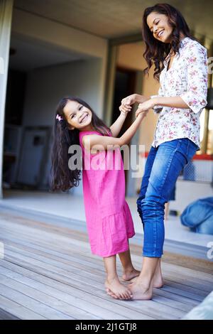 Tanzte mit meiner Tochter. Aufnahme eines niedlichen kleinen Mädchens, das auf den Füßen ihrer Mutter tanzt. Stockfoto