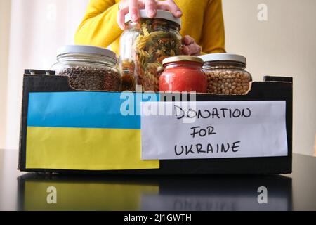 Eine unkenntliche Frau, die Gläser mit Lebensmitteln in eine Schachtel legte, um ukrainischen Flüchtlingen zu spenden. Stockfoto