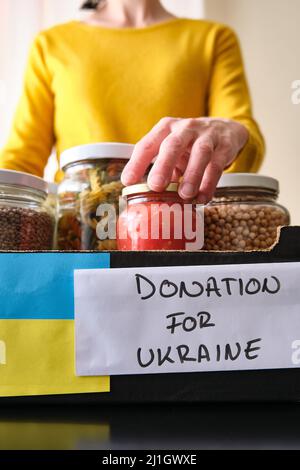 Eine unkenntliche Frau, die Gläser mit Lebensmitteln in eine Schachtel legte, um ukrainischen Flüchtlingen zu spenden. Stockfoto