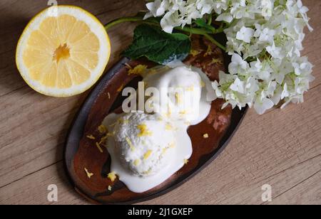 Hausgemachtes Bio-Eis auf dem Tisch in einer handgefertigten Keramikplatte mit einer halben Zitrone und einem Zweig aus weißem Flieder. Stockfoto