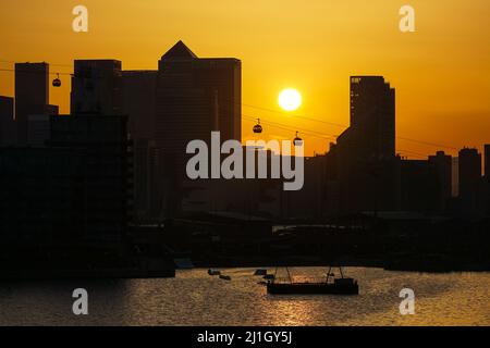 London, Großbritannien. 25. März 2022. Wetter in Großbritannien: Die Sonne geht hinter den Wolkenkratzern von Canary Wharf unter. Quelle: Marcin Rogozinski/Alamy Live News