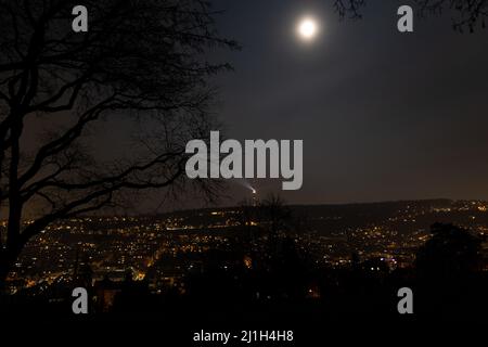 Nachtansicht der Stuttgarter cityline. Fernsehturm mit hellem Lichtstrahl, Vollmond, Äste von Bäumen im Vordergrund Stockfoto