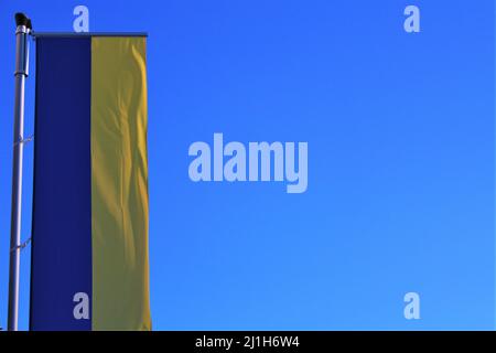 Fahnenmast mit Banner der ukrainischen Flagge, die senkrecht gegen einen klaren blauen Himmel fliegt. Grafische Ressource zur Ukraine mit Platz für Text. Stockfoto