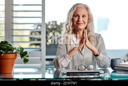 Die Entscheidung, von zu Hause aus zu arbeiten, war die beste Entscheidung überhaupt. Ein Porträt einer attraktiven Geschäftsfrau, die mit ihren Händen zusammen sitzt Stockfoto