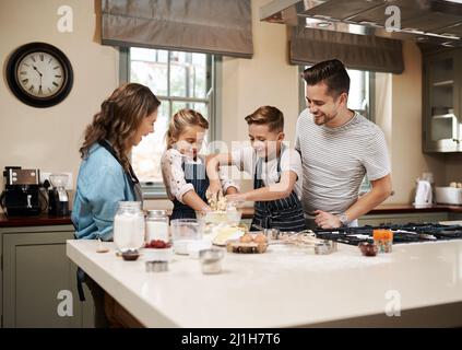 Nichts schmeckt so gut wie etwas, das von der ganzen Familie zubereitet wird. Eine kleine Aufnahme einer jungen Familie, die zu Hause in der Küche backt. Stockfoto