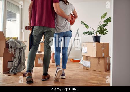 Detail, beschnittenes Bild eines jungen Paares von hinten, das sich gegenseitig hält und in einer neuen Wohnung mit ausgepackten Schachteln um sich herumläuft Stockfoto