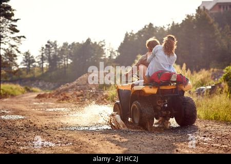 Junges Paar auf einem Offroad-Abenteuer. Mann, der Quad fährt, mit Freundin, die hinter ihm sitzt und die Fahrt im Bergwald genießt. Natur im Freien Stockfoto