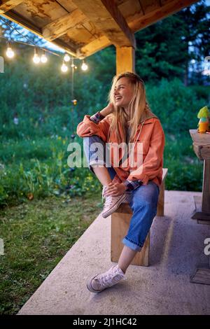 Junge blonde Mädchen genießen schönen Abend vor Holzhütte in der Natur. Ruhe, Urlaub, Urlaubsgekont. Stockfoto