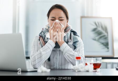 2020, dem Jahr, in dem die Welt krank wurde. Aufnahme einer jungen Geschäftsfrau, die in einem modernen Büro ihre Nase an ihren Schreibtisch bläst. Stockfoto