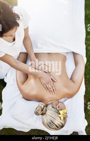 Achte darauf, dass ich wach bleibe. Eine Aufnahme einer entspannten Frau mittleren Alters, die auf dem Bauch liegt, während sie tagsüber eine Massage in einem Spa im Freien erhält. Stockfoto