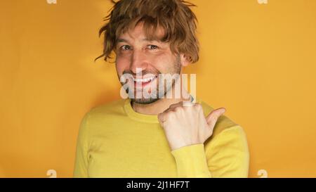 Junger Mann mit einem gelben Hemd, der lächelnd über einem isolierten gelben Hintergrund steht und auf die Kamera blickt, die mit einer Hand und einem Finger auf den zeigt Stockfoto