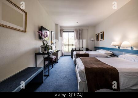 Hotelzimmer mit zwei Kingsize-Betten, Schreibtisch mit Brust, Flachbildfernseher an der Wand und blauem Teppichboden Stockfoto