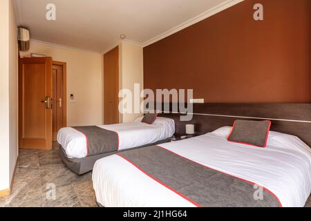 Hotelzimmer mit Twin-Betten mit Holzkopfteil und braunen Kissen mit roten Zierelementen und dunklem Marmorfußboden Stockfoto