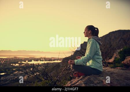 Meditation mit Aussicht. Ganzkörperaufnahme einer sportlichen jungen Frau, die im Freien meditiert. Stockfoto