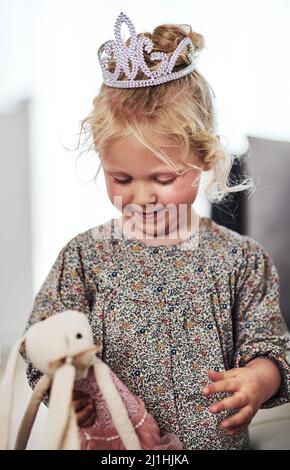 Ich bin die Prinzessin dieses Hauses. Eine kurze Aufnahme eines entzückenden kleinen Mädchens, das allein im Wohnzimmer steht und zu Hause mit ihrem Spielzeug spielt. Stockfoto