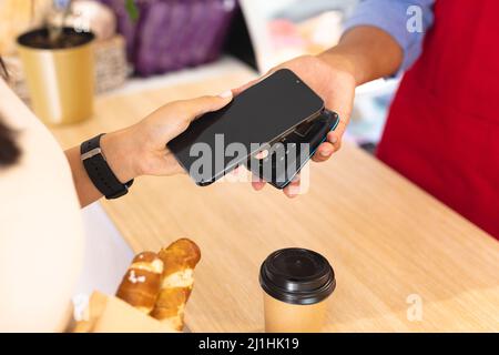 Mittelteil der multirassischen Kunden und Barista tun kontaktlose Zahlung über Smartphone im Café. Unverändert, Café-Kultur, Technologie, Beruf A Stockfoto