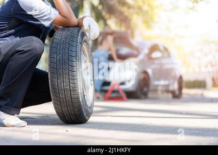 Expertise Mechaniker Mann in Uniform hält einen Reifen für eine Frau zum Austausch Autorad auf der Autobahn, Autoservice, Reparatur, Wartungskonzept zu helfen. Stockfoto