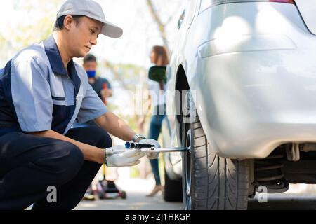 Know-how Mechaniker Mann in Uniform mit Kraft versuchen, die Radschrauben Muttern zu lösen und helfen einer Frau für den Austausch Autorad auf der Autobahn, Car Serv Stockfoto