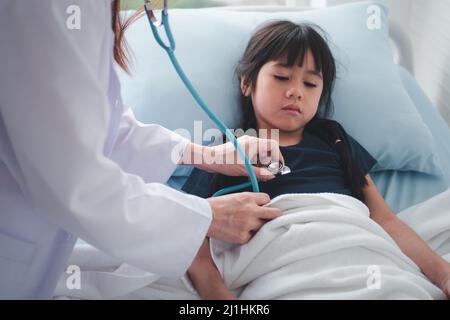 Asiatische Frau Kinderarzt Arzt halten Stethoskop für die Prüfung ein kleines Mädchen Patient und Heck Herzlunge des Kindes, guter Hausarzt Besuch Kind zu Hause Stockfoto