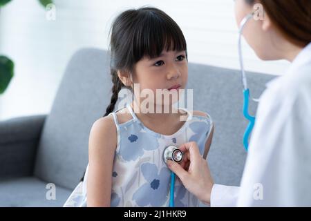 Asiatische Frau Kinderarzt Arzt halten Stethoskop für die Prüfung ein kleines Mädchen Patient und Heck Herzlunge des Kindes, guter Hausarzt Besuch Kind zu Hause Stockfoto