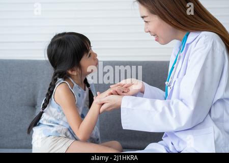 Asiatische Frau Kinderarzt Arzt halten Stethoskop für die Prüfung ein kleines Mädchen Patient und Heck Herzlunge des Kindes, guter Hausarzt Besuch Kind zu Hause Stockfoto