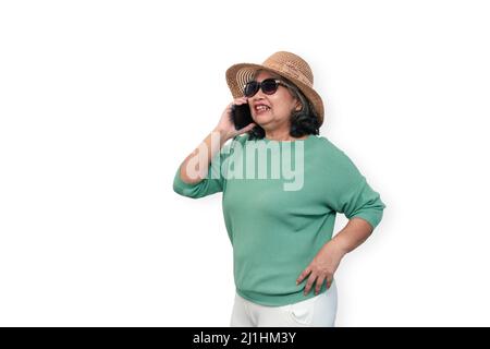 Porträt einer glücklichen asiatischen älteren Frau, die eine Sonnenbrille, einen Hut und ein Smartphone trägt, das isoliert auf weißem Hintergrund steht. Konzept der touristischen genießen Stockfoto