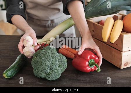 Nahaufnahme einer nicht erkennbaren Frau in der Schürze, die Gemüse auf den Tisch legt, während sie die Holzkiste auspacket Stockfoto