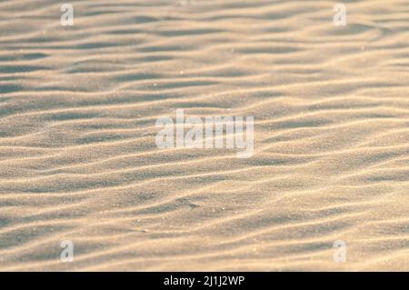 Die pastellfarbene Textur aus feinem Sand am Strand bildet am Abend Wellen Stockfoto