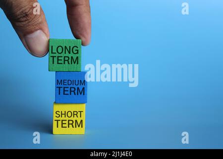 Hand Pick Holzwürfel mit Text LANGFRISTIG auf blauem Hintergrund mit Kopierraum. Investitionskonzept. Stockfoto