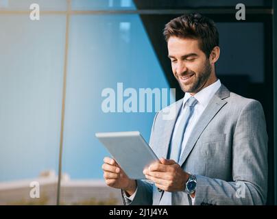 Anschluss an die Stadt. Aufnahme eines hübschen jungen Geschäftsmannes, der vor einem Bürogebäude ein digitales Tablet benutzt. Stockfoto