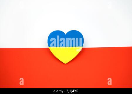 Die Flagge der Ukraine in Form des Herzens auf dem Hintergrund der Flagge Polens. Symbol der Solidarität und Unterstützung. Brüderliche Liebe Stockfoto