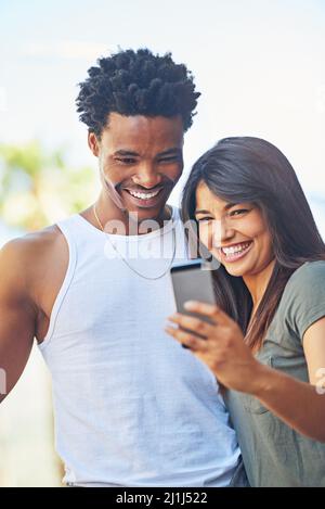 Paar Profilbild. Aufnahme eines glücklichen jungen Paares, das zusammen ein Mobiltelefon benutzt. Stockfoto