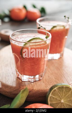 Nahaufnahme von Gläsern erfrischender Zitruscocktails im Sommer mit Limettenscheiben und Zweigen auf Holzbrett Stockfoto