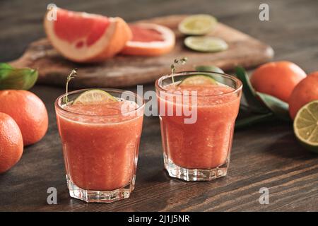 Nahaufnahme von saftigen, erfrischenden Grapefruit-Smoothies mit Limettenscheiben auf dem Esstisch mit Zitrusfrüchten Stockfoto