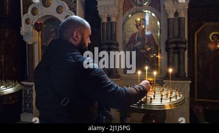 KIEW, UKRAINE 24. FEBRUAR. Ukrainisch-orthodoxer Anhänger zündet Kerzen an, während er in der St.-Wolodymyr-Kathedrale betet, die am 24. Februar 2022 in Kiew, Ukraine, die Mutter-Kathedrale der Ukrainisch-Orthodoxen Kirche – des Kiewer Patriarchats ist. Russland begann einen großen Angriff auf die Ukraine, nachdem das russische parlament Verträge mit zwei abtrünnigen Regionen in der Ostukraine gebilligt hatte. Stockfoto