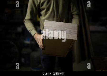 Schachtel Holz in der Hand. Die Produktion der Möbel aus den Brettern. Holzschrank. Einzelheiten der Arbeit. Ergebnis der Plattenbearbeitung. Stockfoto