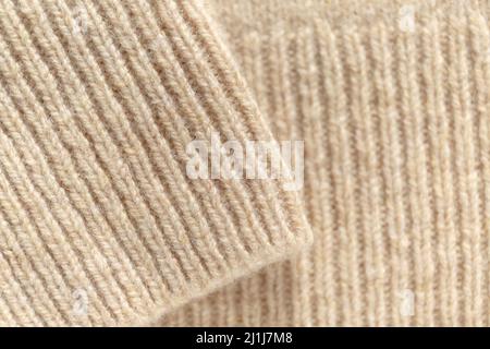 Ein gefaltetes Kaschmir-Strickpullover in einem beigefarbenen Farbton. Strickpullover aus Wolle, strukturierter Hintergrund. Stylische Strickmode für die Herbst-Winter-Saison. Stockfoto