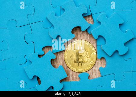 Blaues Puzzle-Muster mit goldenem Bitcoin darunter. Stockfoto