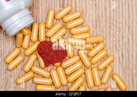 Rotes Herz, umgeben von gelben Pillen. Pillen der Liebe.Rotes Herz mit Pillen auf dem Tisch. Stockfoto