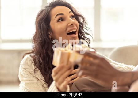 Ein glückliches Paar von Mulattoes tauschen Geschenke miteinander aus. Gemeinsame Familienfeiern Stockfoto