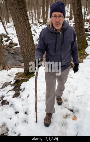 Gesunder älterer Mann mit Spazierstock Wanderungen durch verschneite Pennsylvania Wälder Stockfoto