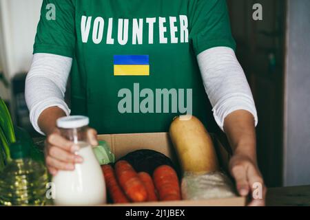 Volunteer bereitet Nahrungsmittelbox für ukrainische Kriegsflüchtlinge vor - Focus on ukraine flag Stockfoto