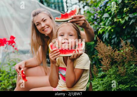 Glückliche Mutter und Tochter essen Wassermelone und Spaß im Freien im Sommer Tag. Feiertage Stockfoto