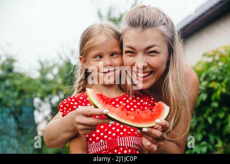 Glückliche Mutter und Tochter essen Wassermelone und Spaß im Garten. Stockfoto