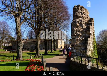 Menschen entspannen, Wandern auf Wegen in sonnigen Park (helle Border Blumen, alte Ruinen, blauer Himmel) - Knaresborough Castle, North Yorkshire, England, Großbritannien. Stockfoto